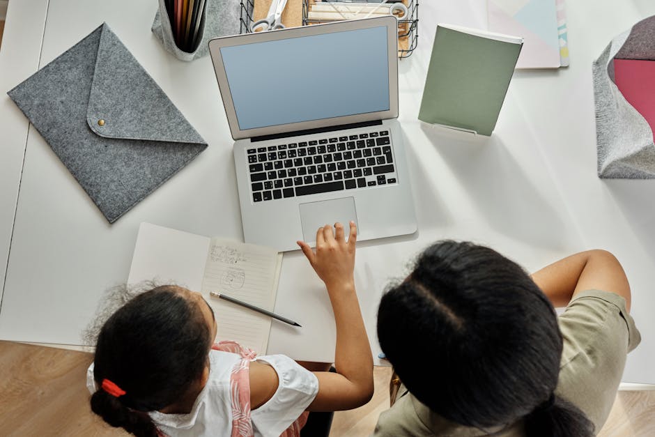 A mother helps her daughter with schoolwork on a laptop at home, promoting education and bonding